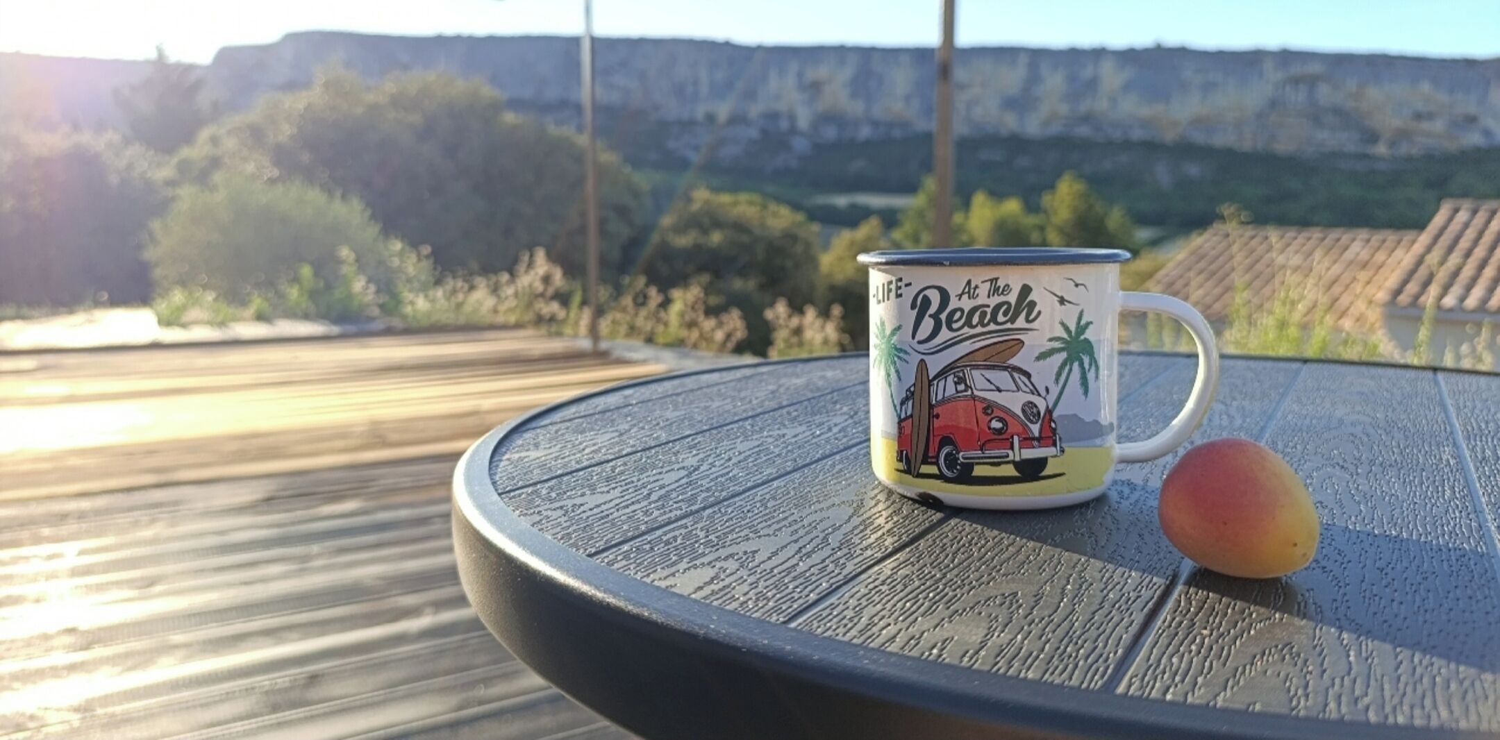 Una mesa con una taza que muestra una escena de playa y un melocotón.