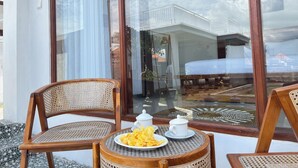 Een balkon met rieten stoelen en een klein rond tafeltje met een schaal lekkernijen en twee witte bekers.
