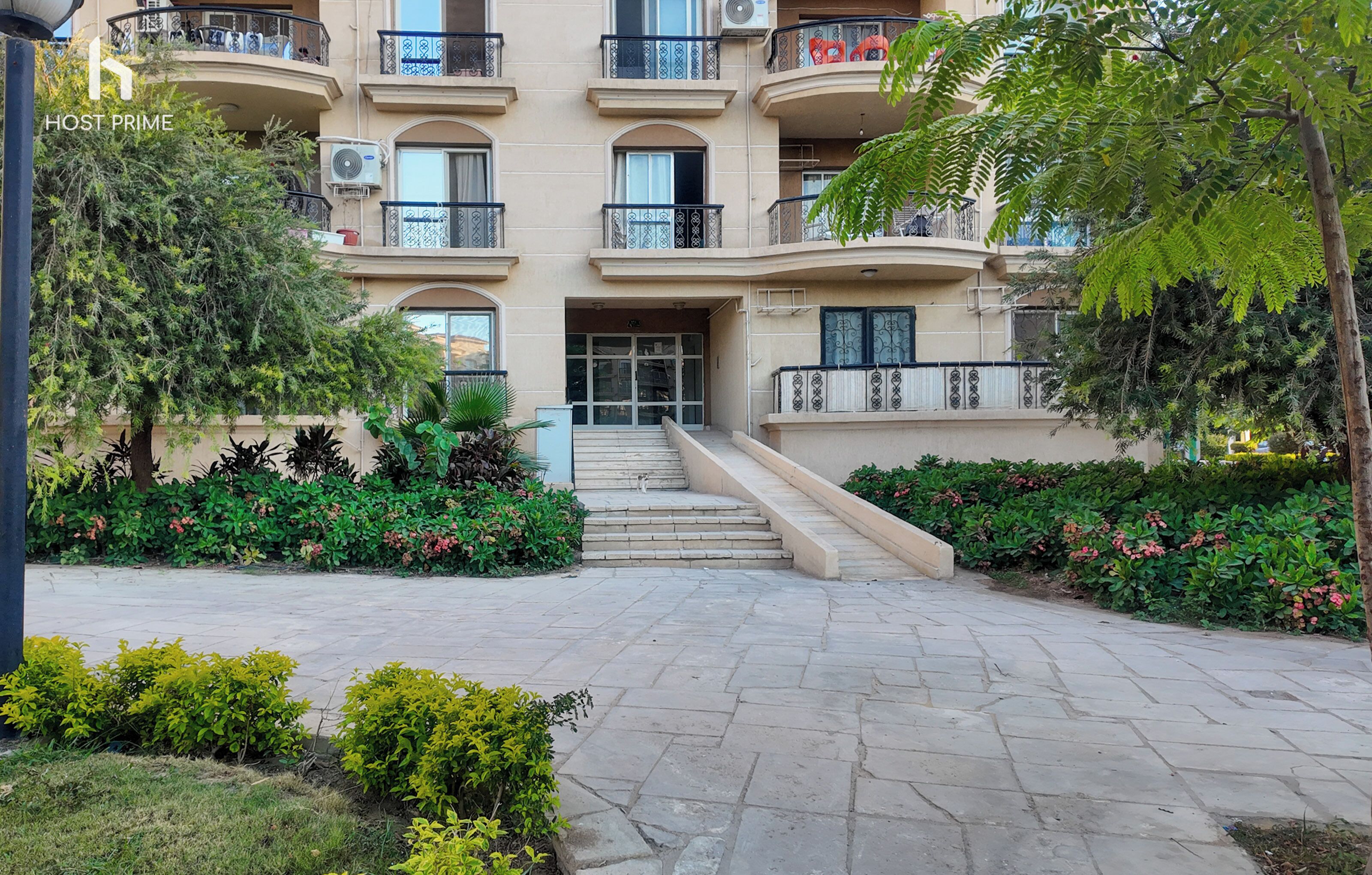A multi-story hotel with a central entrance, outdoor seating area, and a staircase leading to the entrance.
