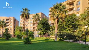 Edifício residencial com várias varandas, cercado por vegetação exuberante e palmeiras.