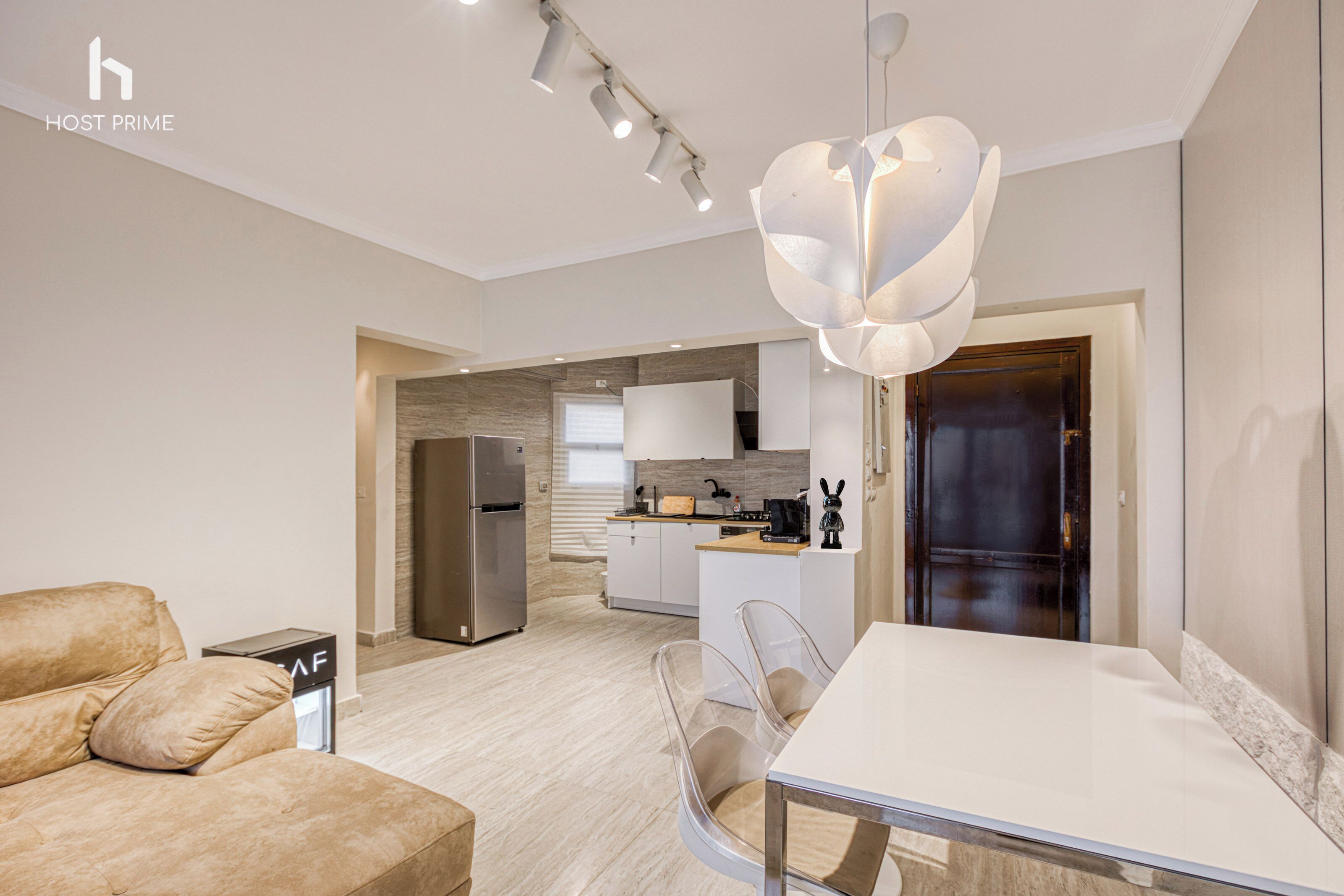 A modern living room with a sofa, a dining table, and a kitchen in the background.