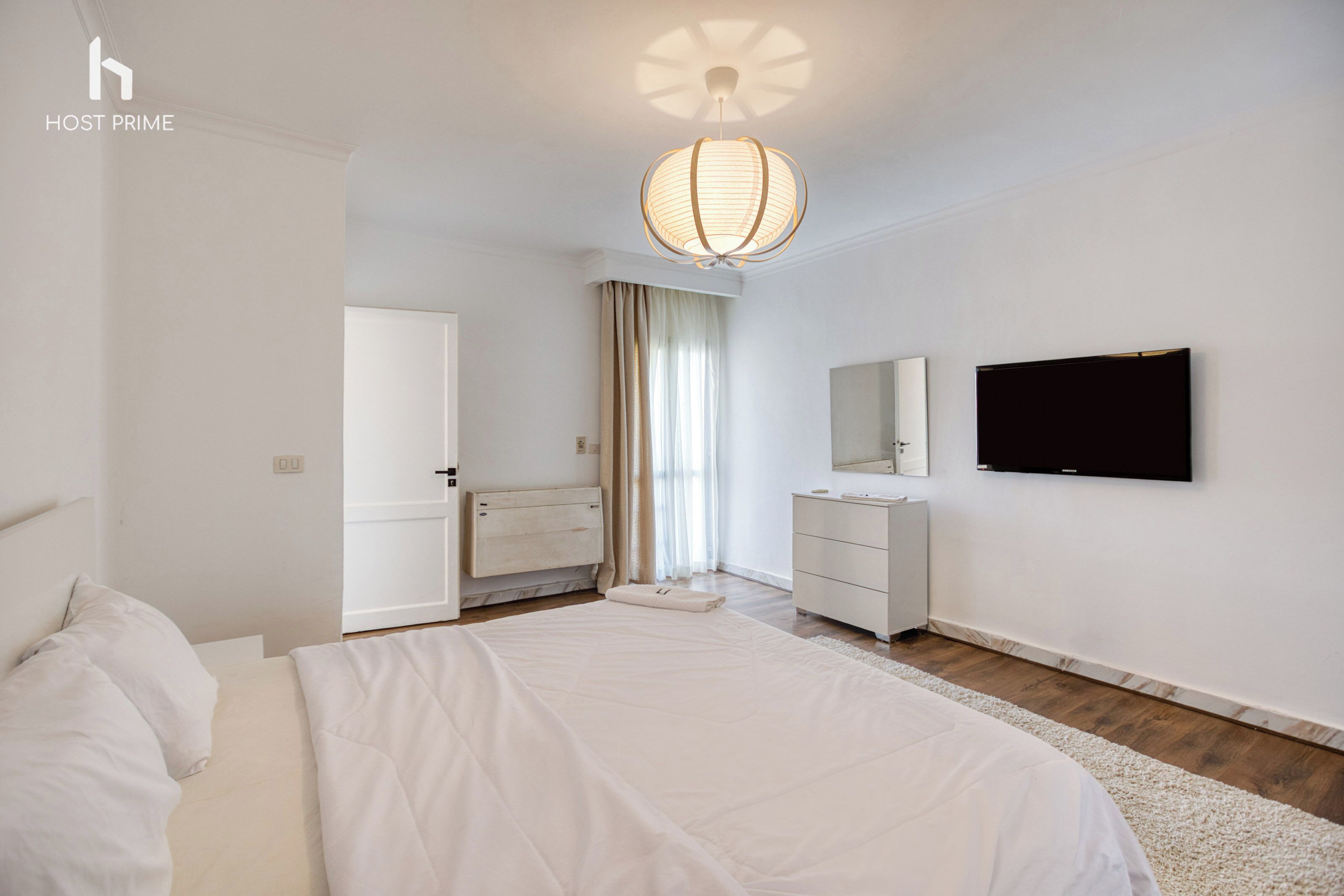 A modern hotel room with a large bed, a dresser, a television mounted on the wall, and a ceiling light fixture.