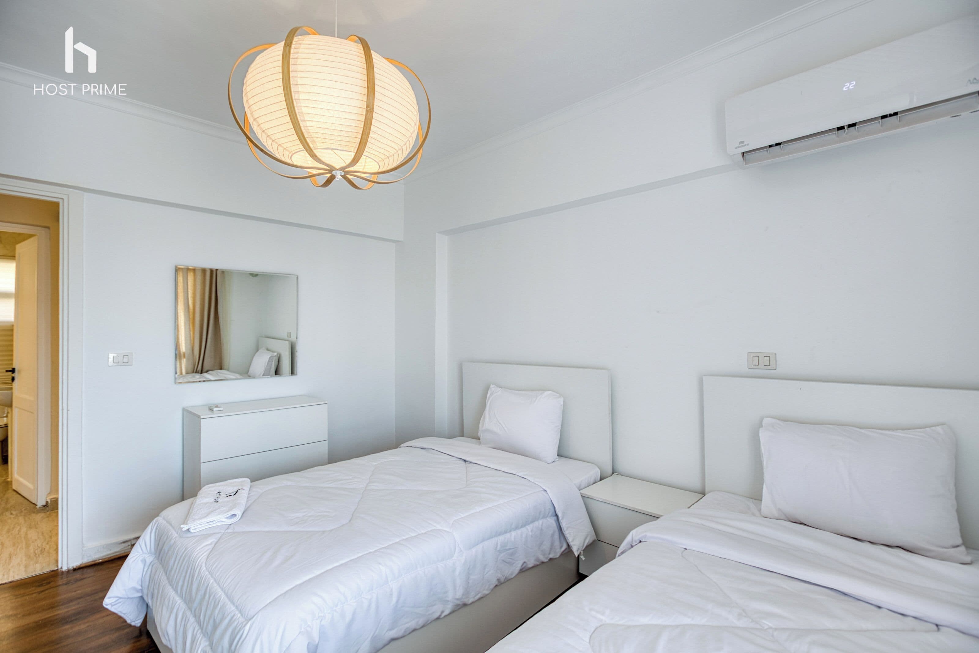 Habitación de hotel con dos camas, una mesita de noche, un espejo y una lámpara colgante.