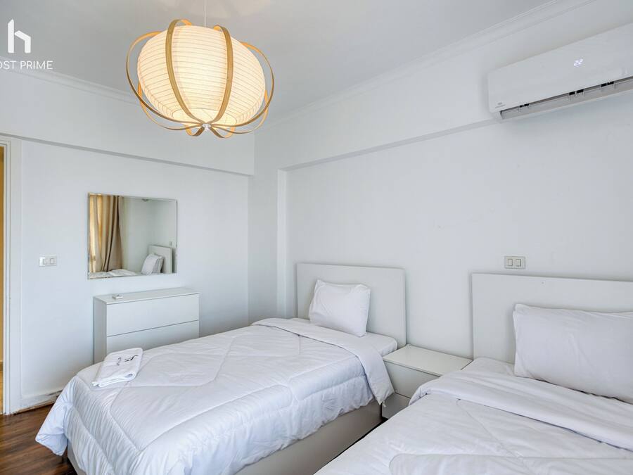 Habitación de hotel con dos camas, una mesita de noche, un espejo y una lámpara colgante.