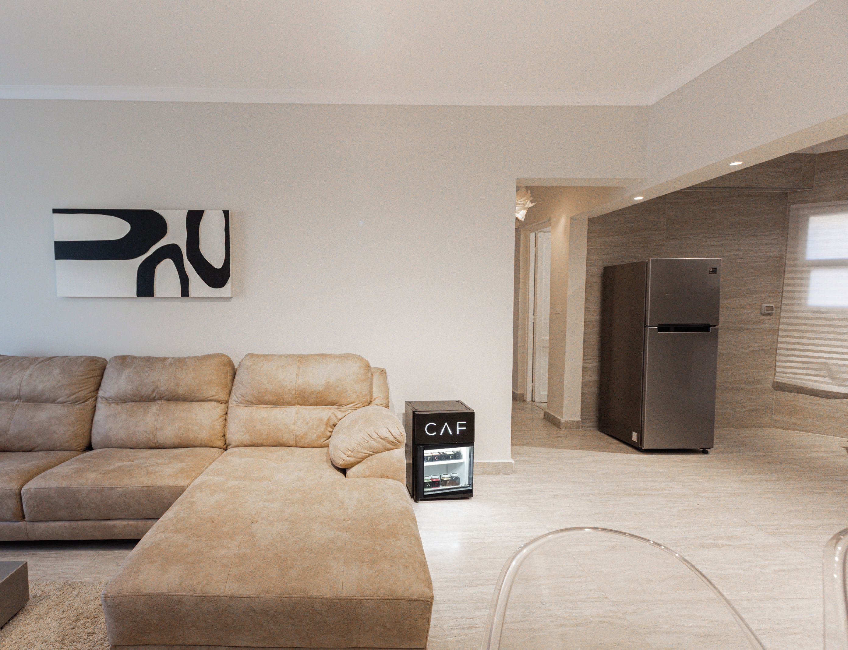 Un salon moderne avec un canapé d’angle, un réfrigérateur encastré et un design minimaliste.