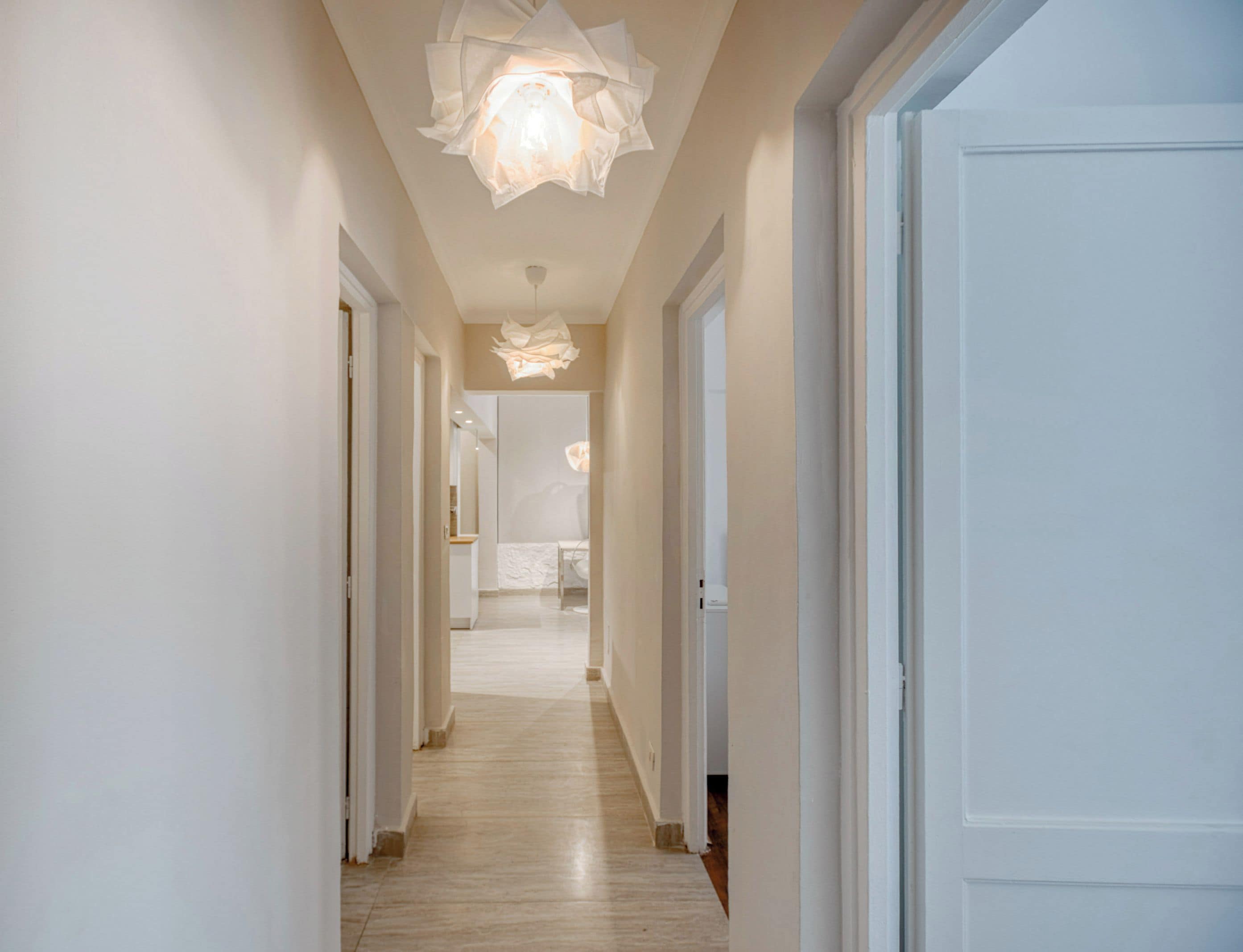 Un pasillo con paredes blancas y piso de madera que conduce a una habitación con una cama y una mesita de noche.