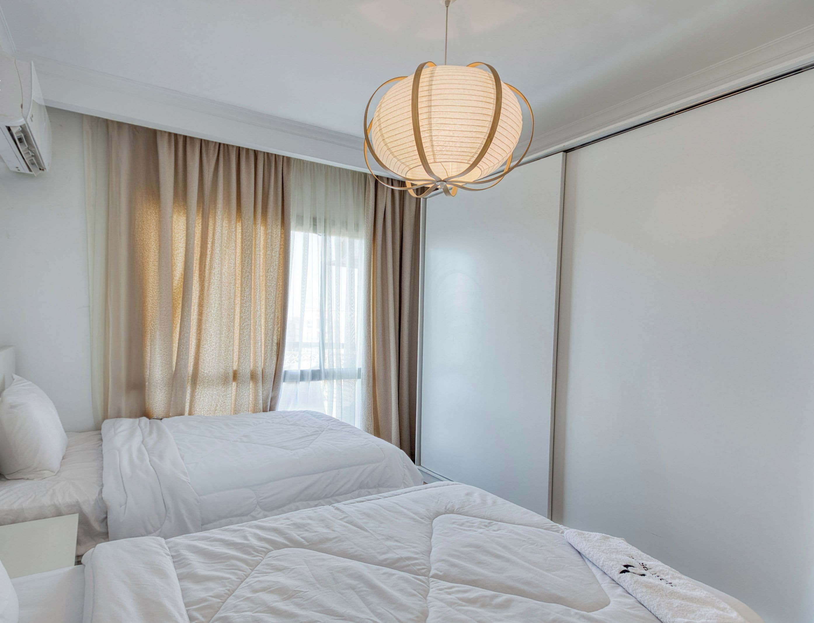 A hotel room with a bed, a bedside table, a hanging light fixture, and a window with curtains.