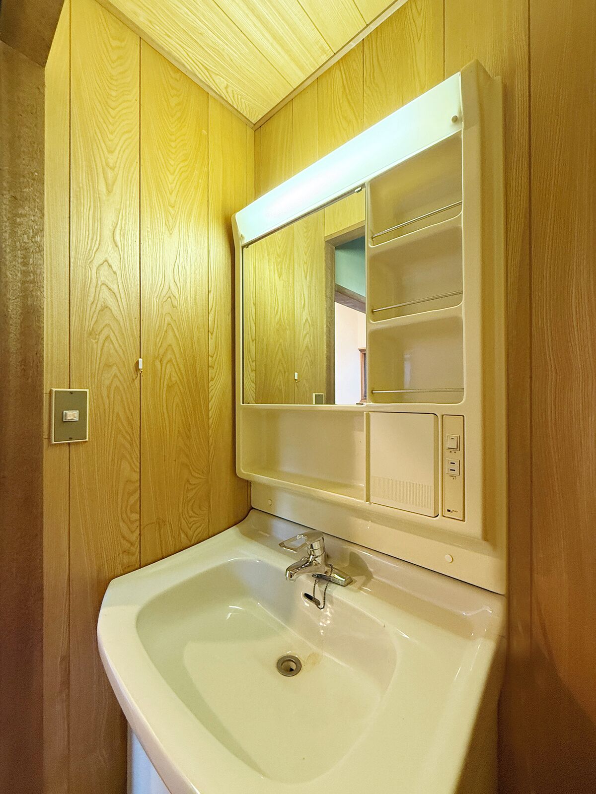 Une salle de bain avec un lambris en bois, un lavabo blanc, un miroir et une étagère contenant des articles de toilette.