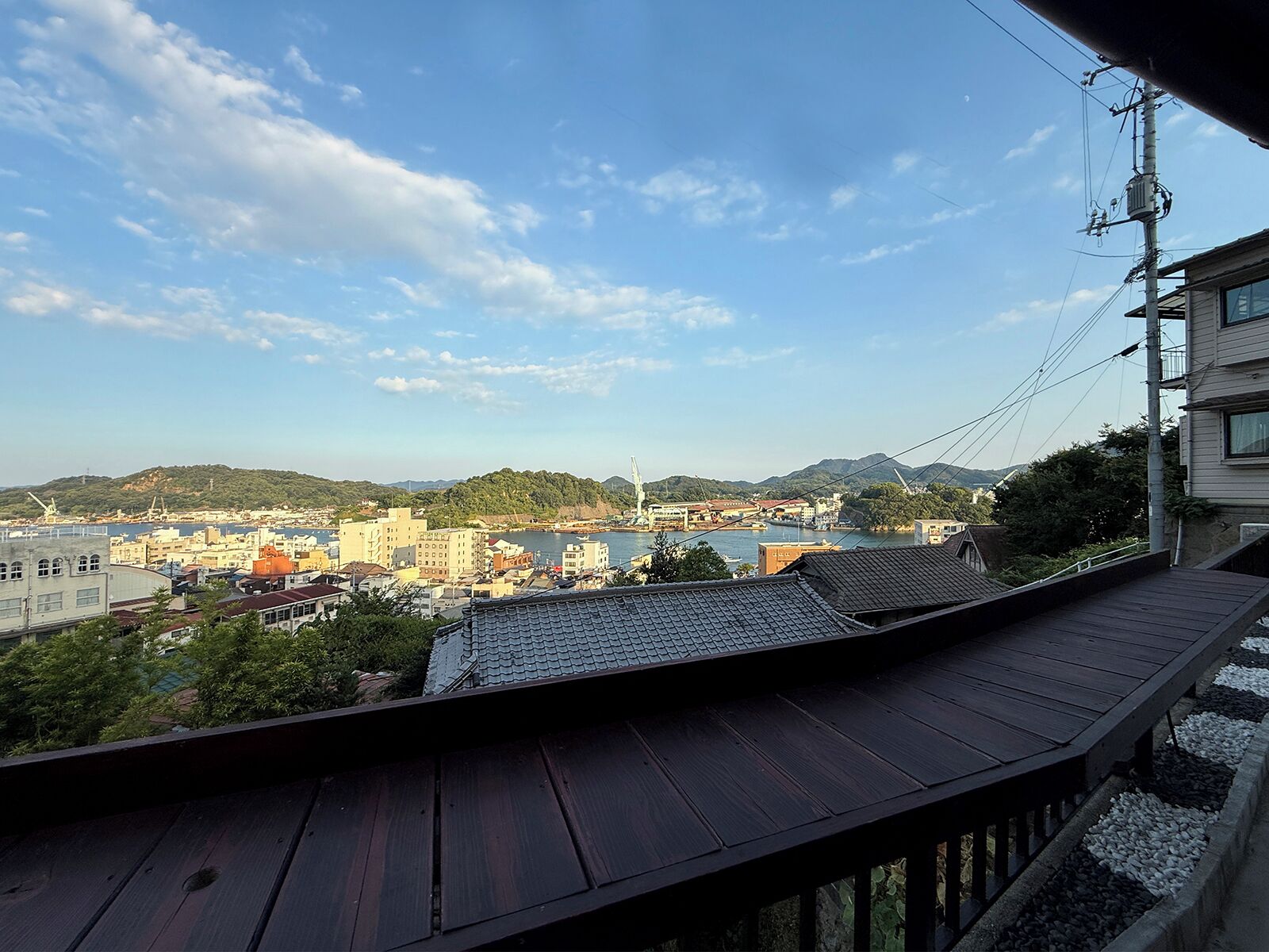 Vista de uma varanda com vista para a paisagem urbana, com edifícios, um corpo d'água e colinas ao longe.