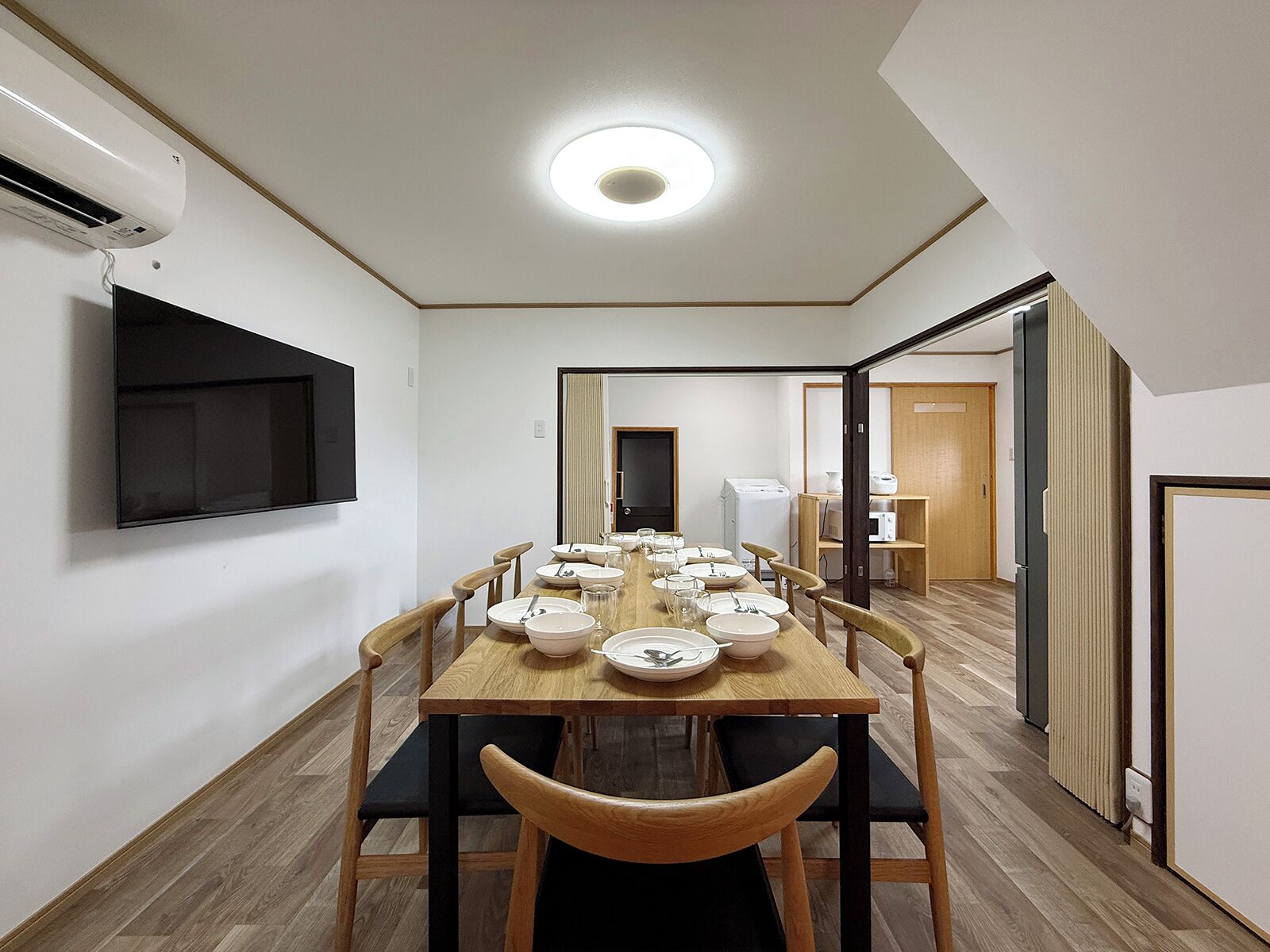 A dining area with a long table, chairs, and a TV mounted on the wall.
