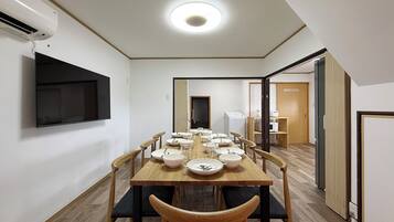 A dining area with a long table, chairs, and a TV mounted on the wall.