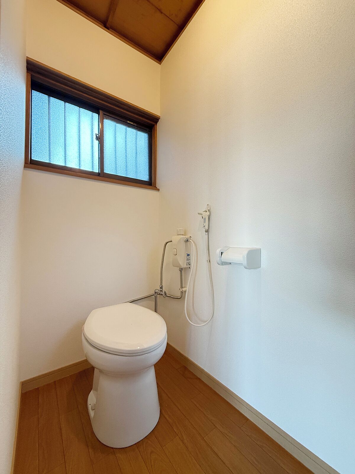 A small, compact bathroom with a toilet, a window, and a shower unit.