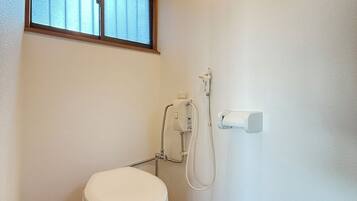 A small, compact bathroom with a toilet, a window, and a shower unit.