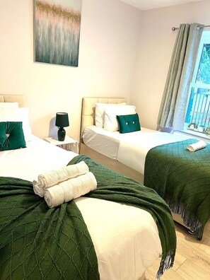 A hotel room with two beds, a nightstand, a lamp, and a window with curtains.