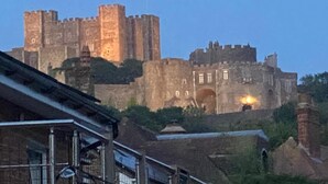 A historic castle with multiple towers and a flag, surrounded by greenery and residential buildings. - Dover Ferry Luxury Apartments (Kent)