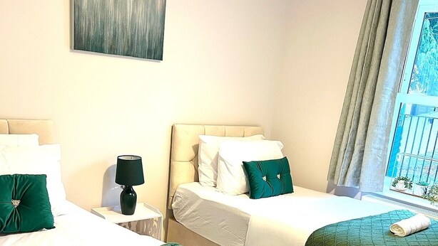 A hotel room with two beds, a nightstand, a lamp, and a window with curtains.