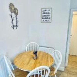 Une table ronde en bois, des chaises blanches, un panneau fixé au mur et une plante décorative.