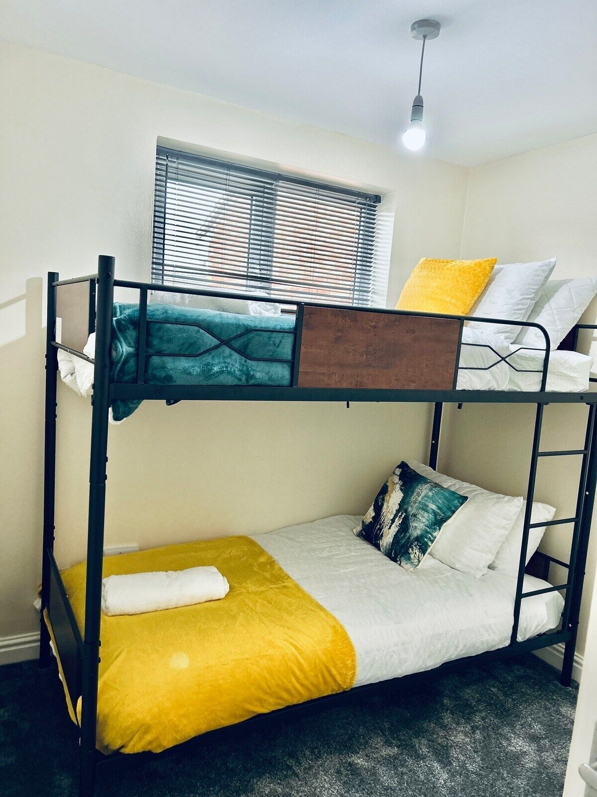 A bunk bed room with a window, a light fixture, and a bed with a yellow blanket.