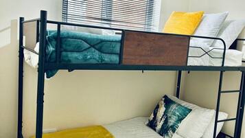 A bunk bed room with a window, a light fixture, and a bed with a yellow blanket.