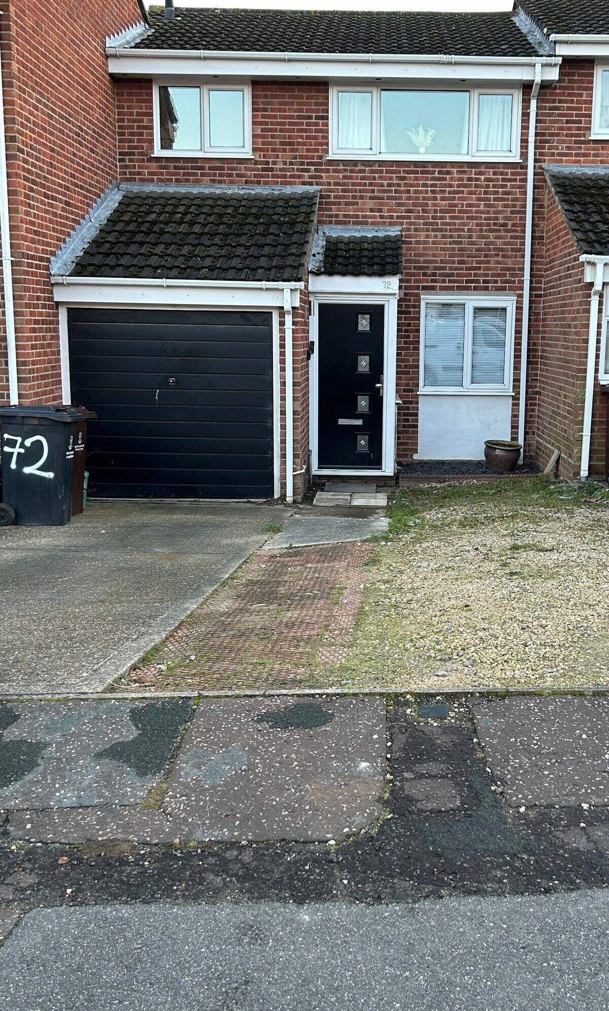 Et toetagers murstenshus med garage, hoveddør og en lille forhave.