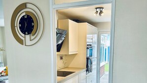 A modern kitchen with white cabinets, a black countertop, and a clock on the wall. - Holiday Home with Parking , Near Colchester Zoo (Essex)