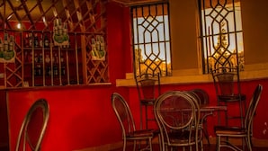 A bar area with metal chairs and tables, a red wall, and a window with a metal grille. - Katani Resort  (Mlolongo)