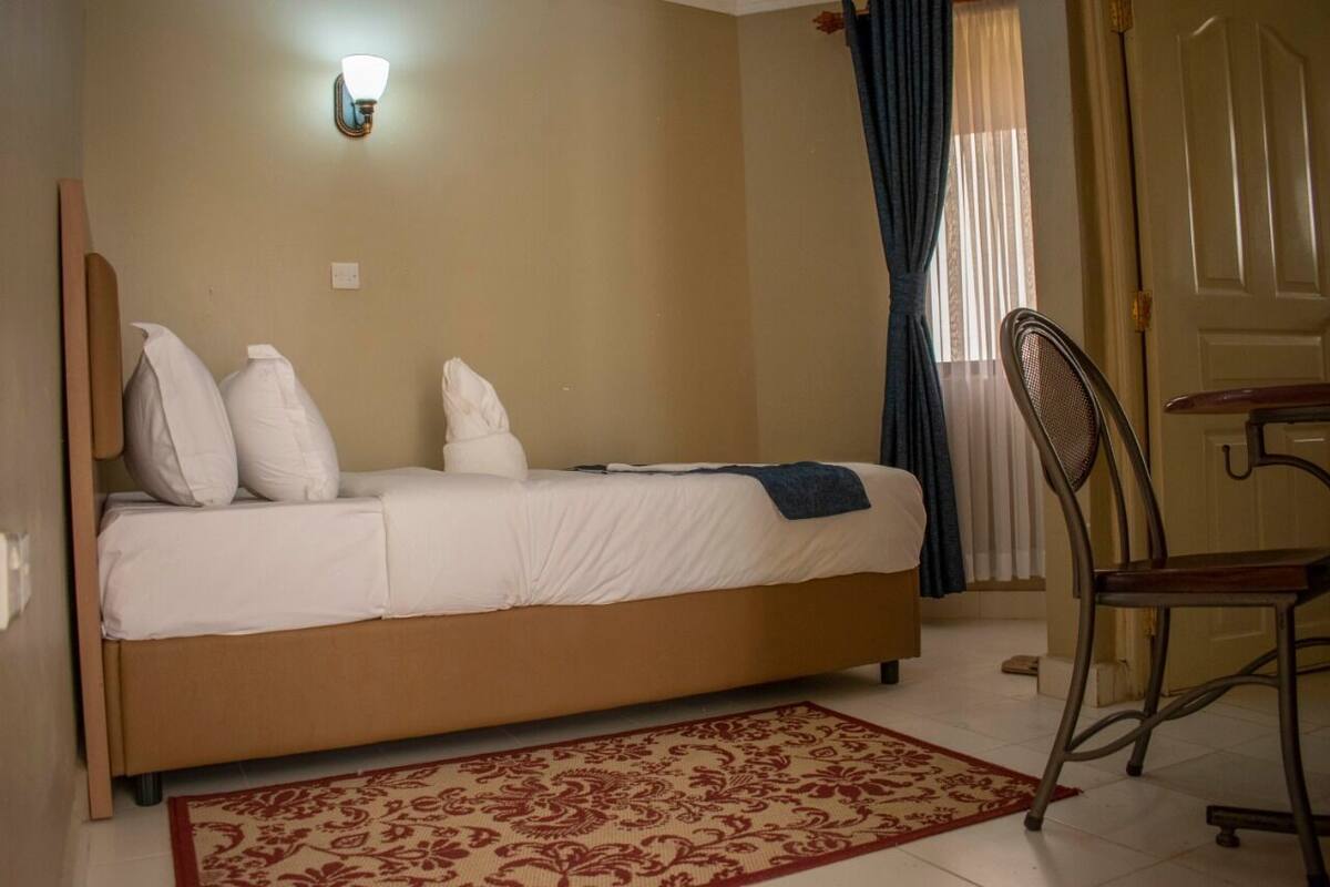 A single bed with a headboard, a bedside table, a chair, and a patterned rug.