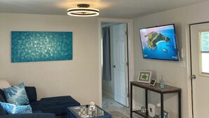 A living room with a dark blue sofa, a glass coffee table, a wall-mounted TV, and a patterned rug. - Lovely 2-bedroom mobile home with AC in Okeechobee, on the canal near the locks. (Okeechobee)