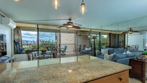 A kitchen with granite countertops, a ceiling fan, and a large window overlooking a patio area.