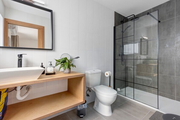 Un baño moderno con lavamanos, inodoro y ducha con mampara de vidrio.
