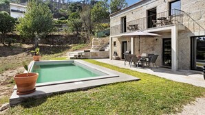 Ein Pool mit Steinbord, eine Terrasse mit Gartenmöbeln und ein Steinhaus mit Balkon.