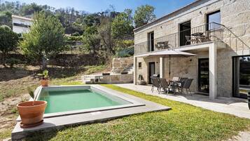 A pool with a stone border, a patio with outdoor furniture, and a stone building with a balcony.