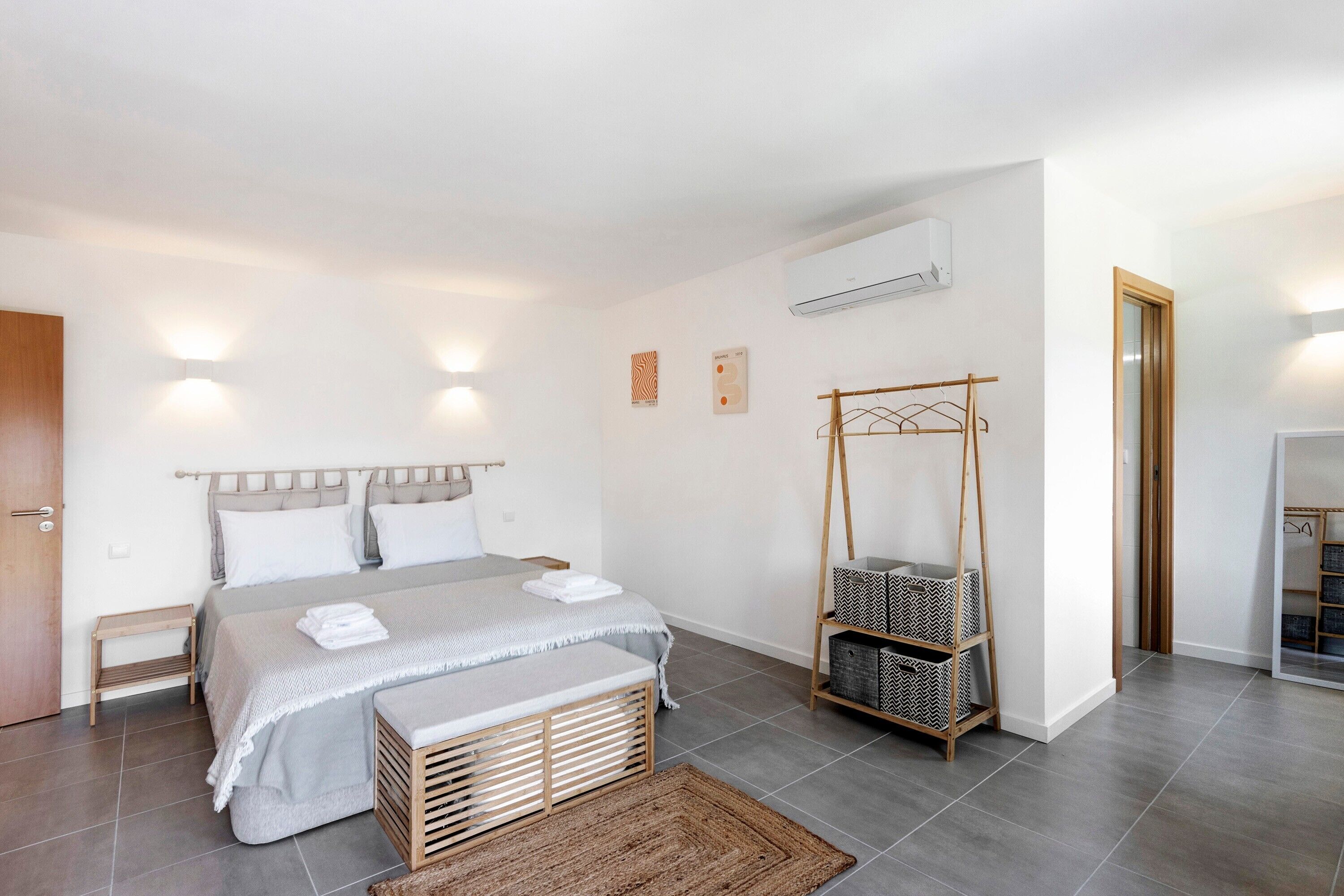 A modern bedroom with a bed, bedside tables, a wooden bench, a hanging rack, and a wardrobe.