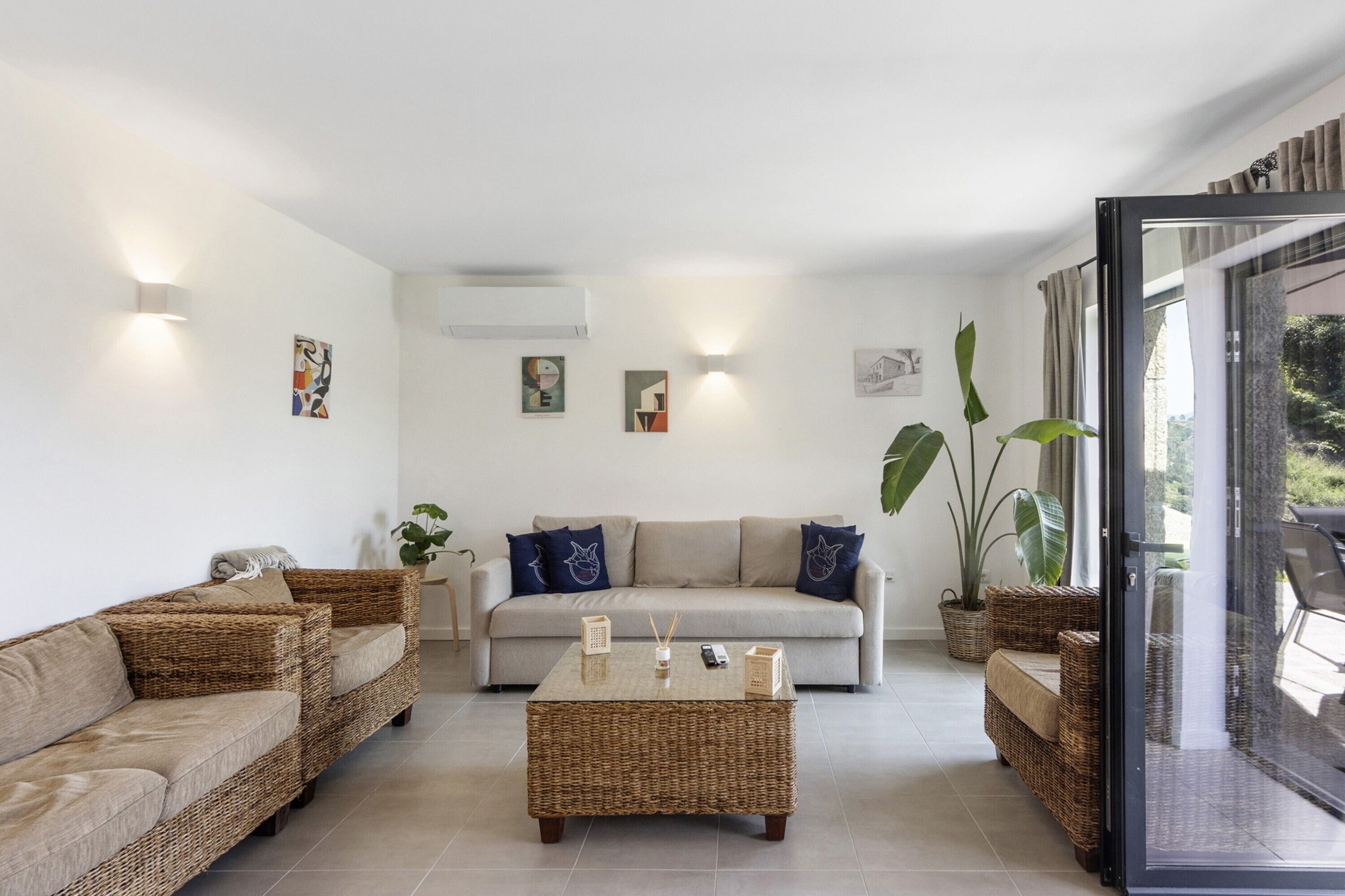 Una sala de estar con un sofá, dos sofás de mimbre, una mesa de centro y un ventanal con cortinas.