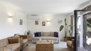Ein Wohnzimmer mit einer Couch, zwei Korbsesseln, einem Couchtisch und einem großen Fenster mit Vorhängen.