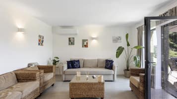 Una sala de estar con un sofá, dos sofás de mimbre, una mesa de centro y un ventanal con cortinas.