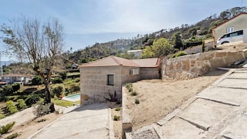Una propiedad residencial con un muro de piedra, un edificio pequeño con techo de tejas y una zona pavimentada con piscina.
