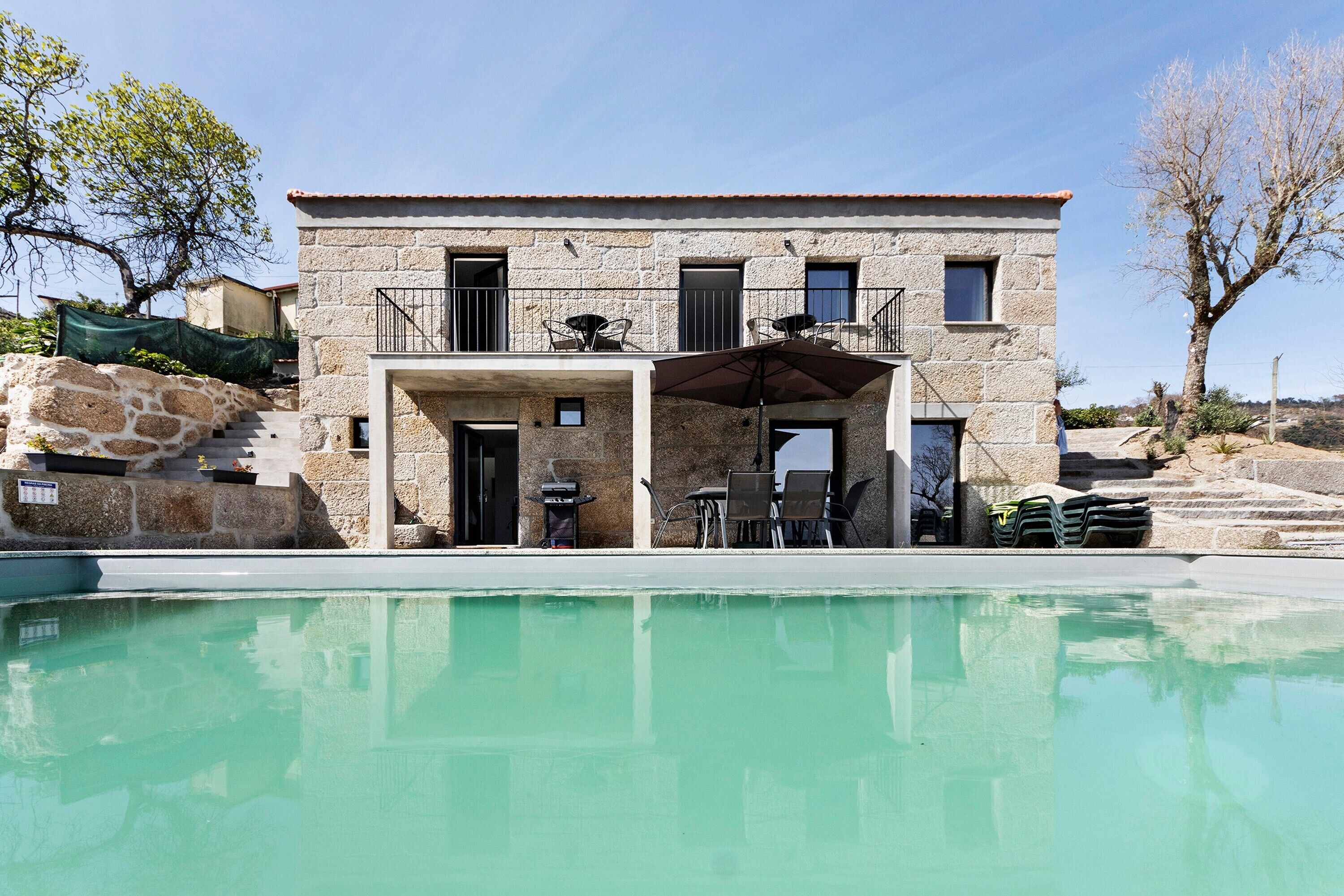 A stone building with a pool, outdoor seating, and a staircase leading to a balcony.