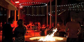An outdoor dining area with a fire feature, string lights, and a crowd of people.