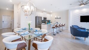 A modern kitchen with white cabinets, stainless steel appliances, and a dining area with a glass table and white chairs. - Glamorous Townhouse 4Bed/3Bath/Pool/5Min Disney (Kissimmee)