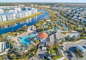 Eine Luftaufnahme eines Resorts mit mehreren Schwimmbecken, einem zentralen Gebäude mit rotem Dach und einem Gewässer.