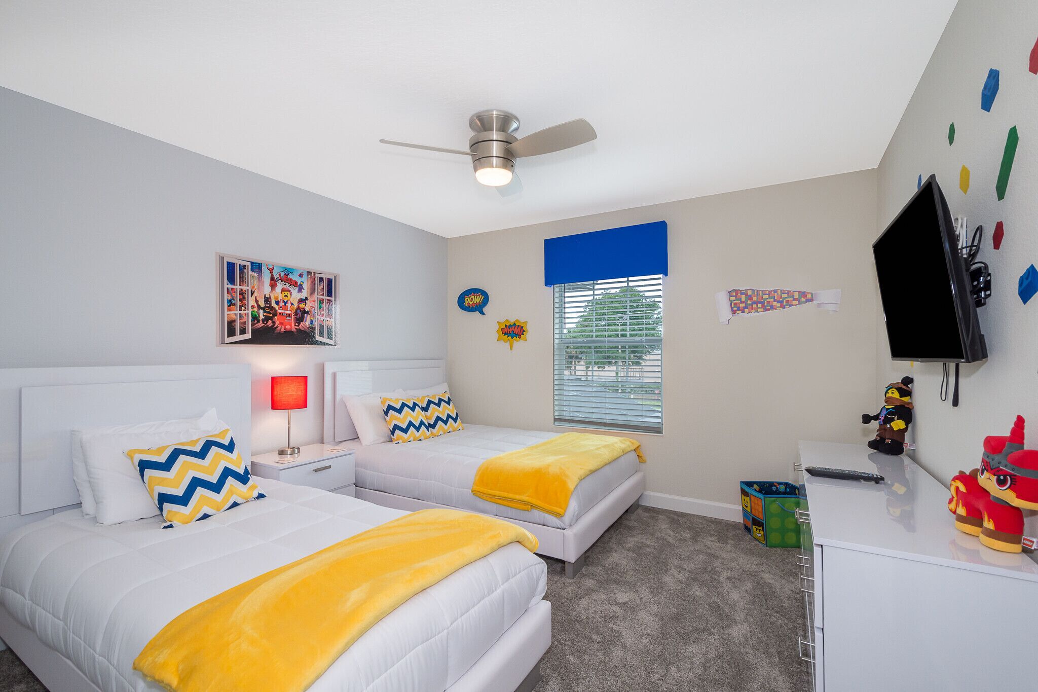 A bedroom with two beds, a ceiling fan, a window with blinds, a TV, and a small desk.