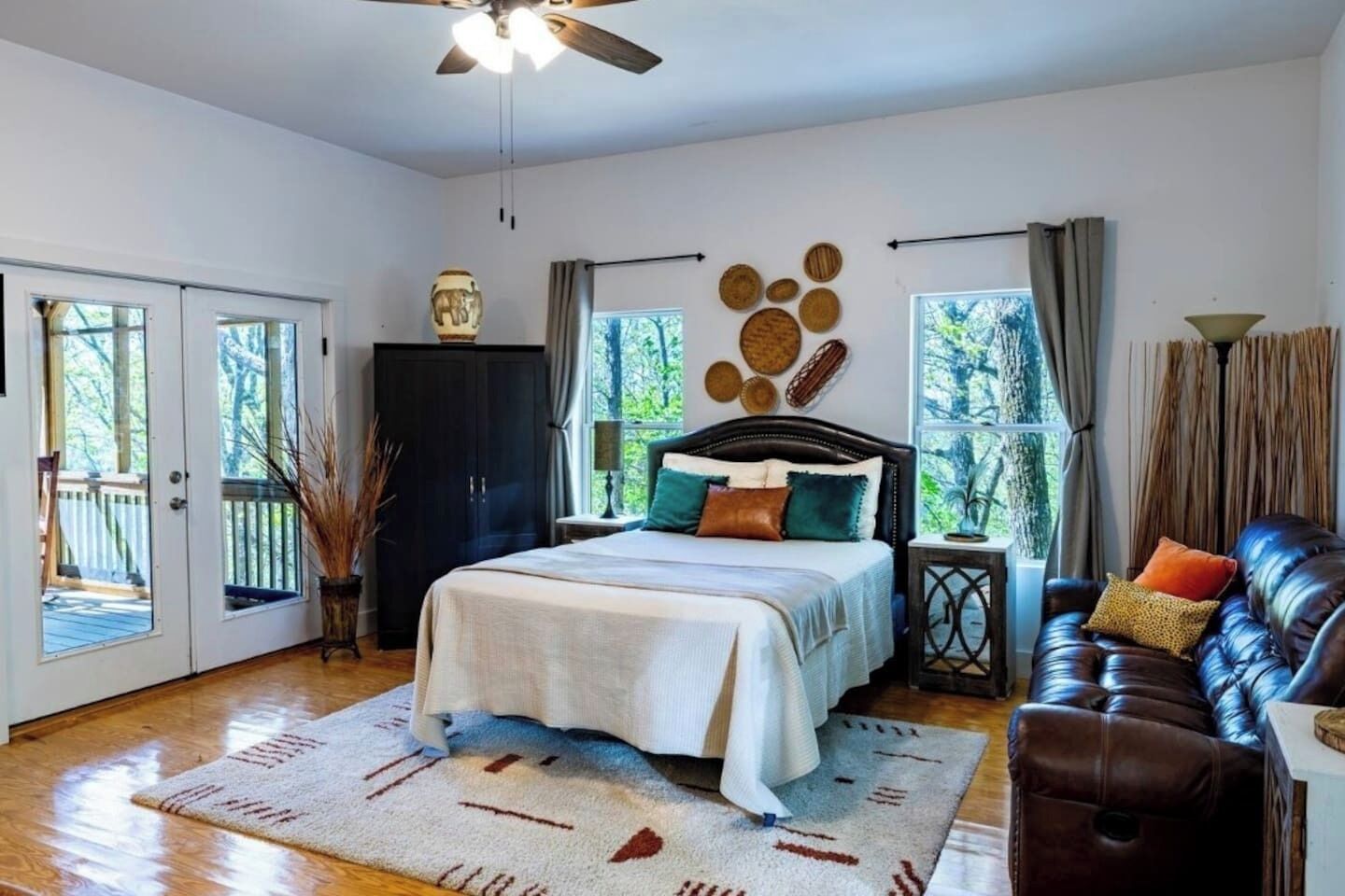 A bedroom with a bed, a leather sofa, a ceiling fan, and a view of the outdoors.