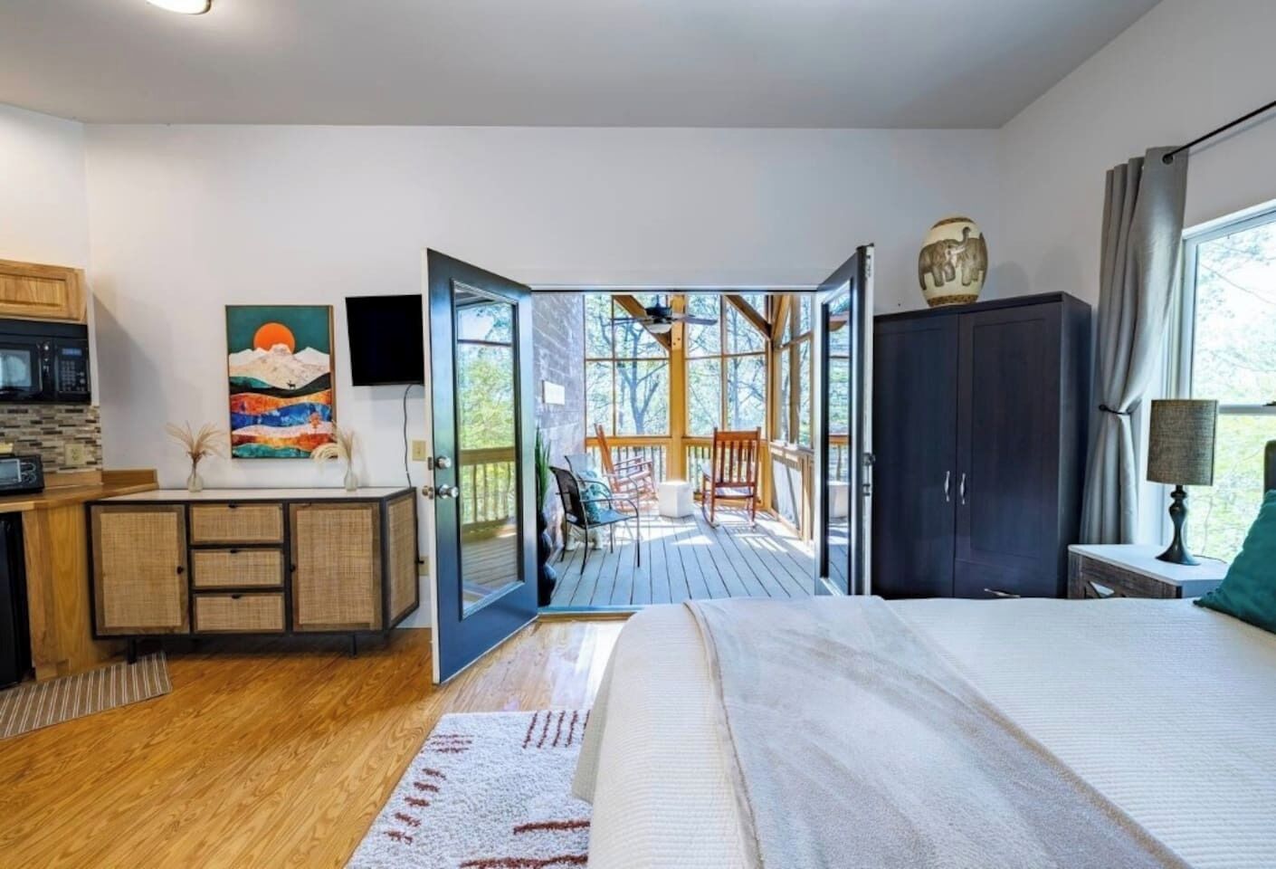 Une chambre avec un grand lit, un bureau avec une chaise, une armoire et une vue sur une terrasse extérieure.