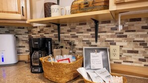 A kitchen area with a coffee maker, a basket of toiletries, and a welcome sign.