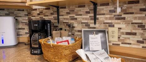 Una cocina con cafetera, un cesto de artículos de aseo y un cartel de bienvenida.