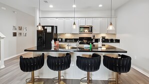 A modern kitchen with white cabinets, a black refrigerator, and a central island with bar stools. - 4BR Solterra Villa with Private Pool (Davenport)