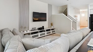 A modern living room with a large flat-screen TV mounted on the wall, a white entertainment unit, and a staircase leading to another level. - 4BR Solterra Villa with Private Pool (Davenport)