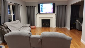 A living room with a fireplace, grey curtains, a sofa, and a television. - Walking distance Golf Course 4-bedroom house with Living  Dining and Family Room (Farmingdale)