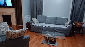 A living room with a grey sofa, a glass coffee table, and a television on a stand. - Walking distance Golf Course 4-bedroom house with Living  Dining and Family Room (Farmingdale)